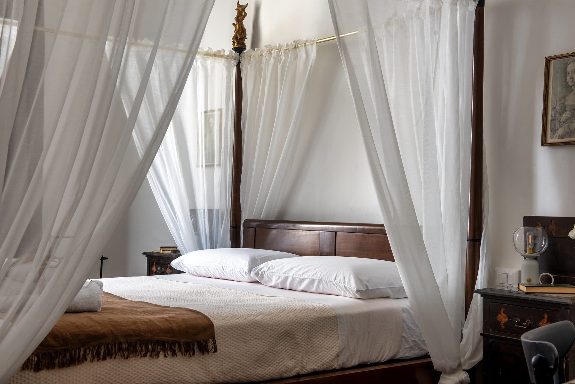 Il letto a baldacchino con le tende bianche e i comodini d'epoca